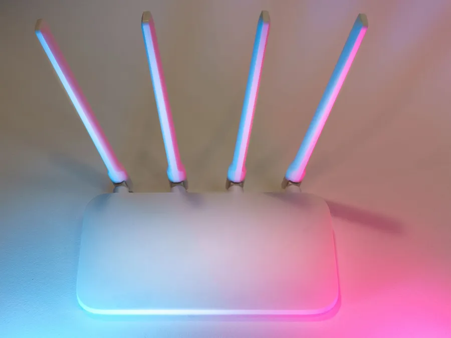 White wireless router with four upright antennas, lit by soft pink and blue light